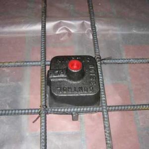 A floating-floor isolation mount set into steel reinforcement mesh over a membrane, before the concrete slab is poured.