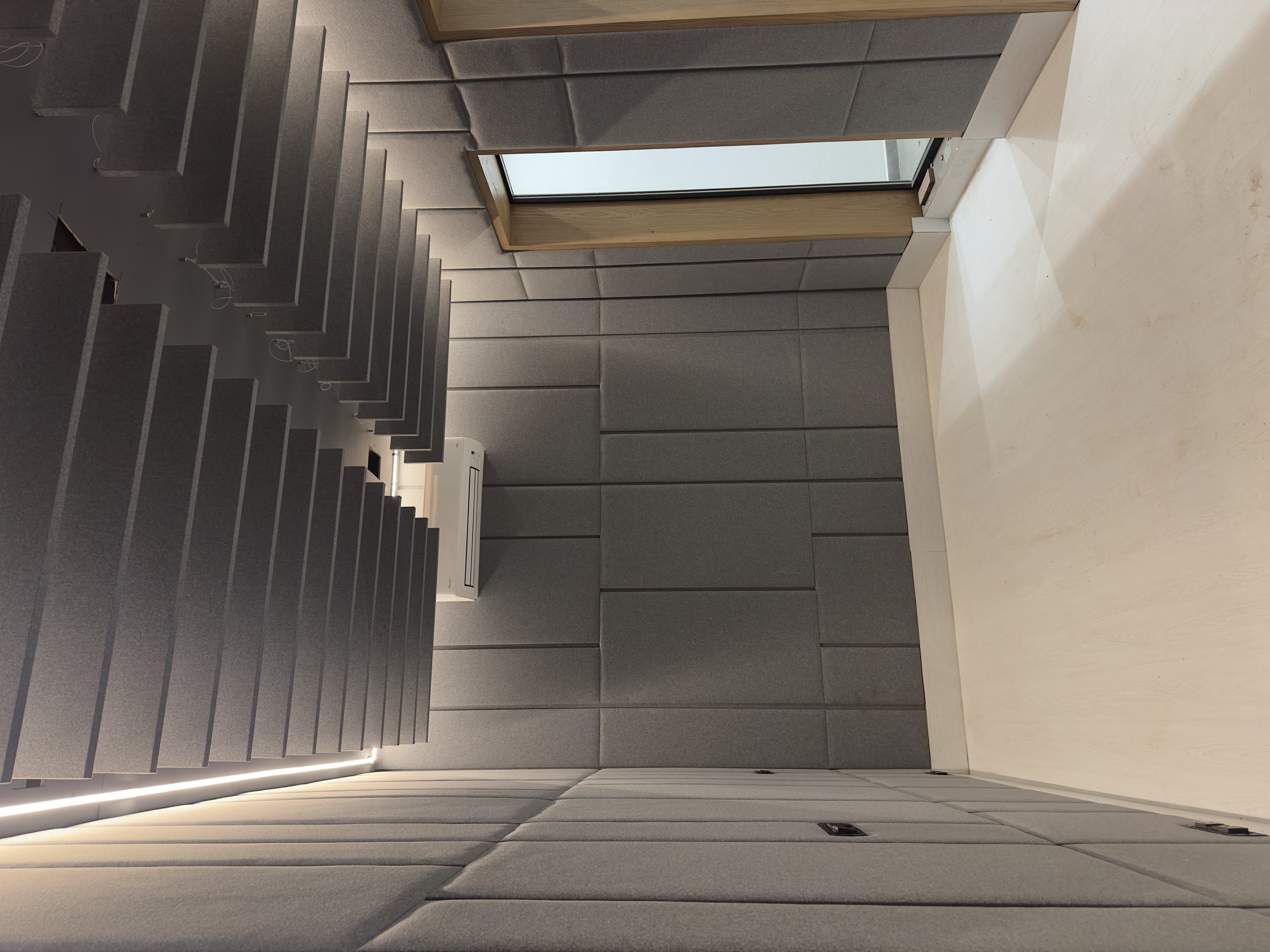 The finished studio: fabric-wrapped panels over the walls, staggered absorbent baffles across the ceiling, and a glazed timber door into the room.